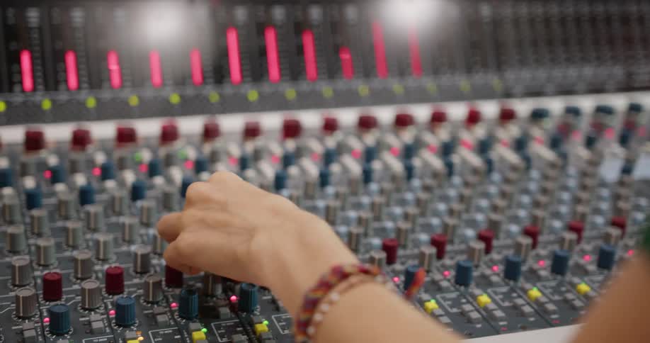 A woman sits in front of a studio mixing board to produce music
