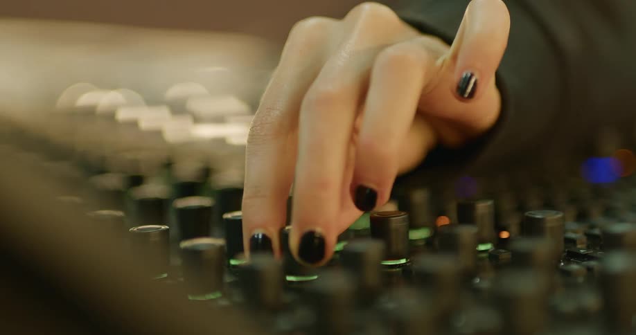 Woman with black fingernails turning knobs on a mixing board
