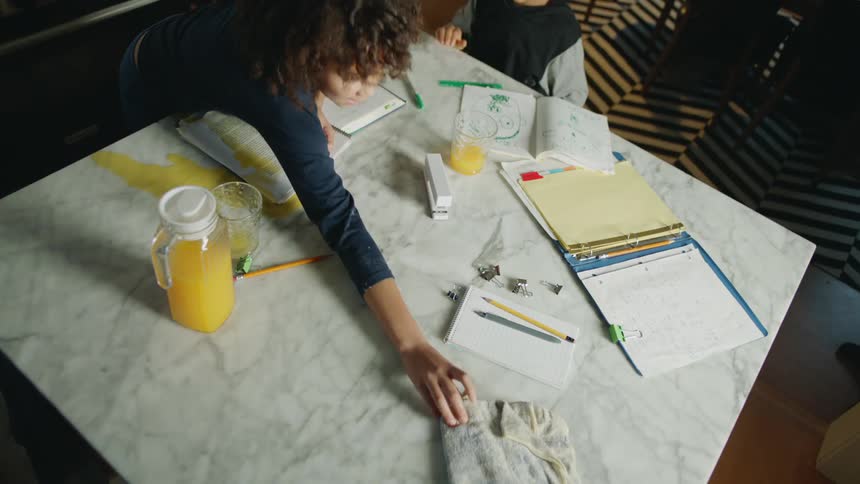 Girl doing homework with her brother spills orange juice over her notebook