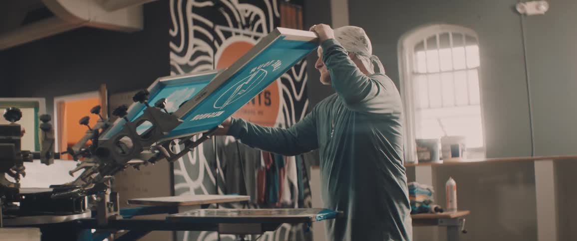 Worker places a screen over a screen printing machine inside a workshop