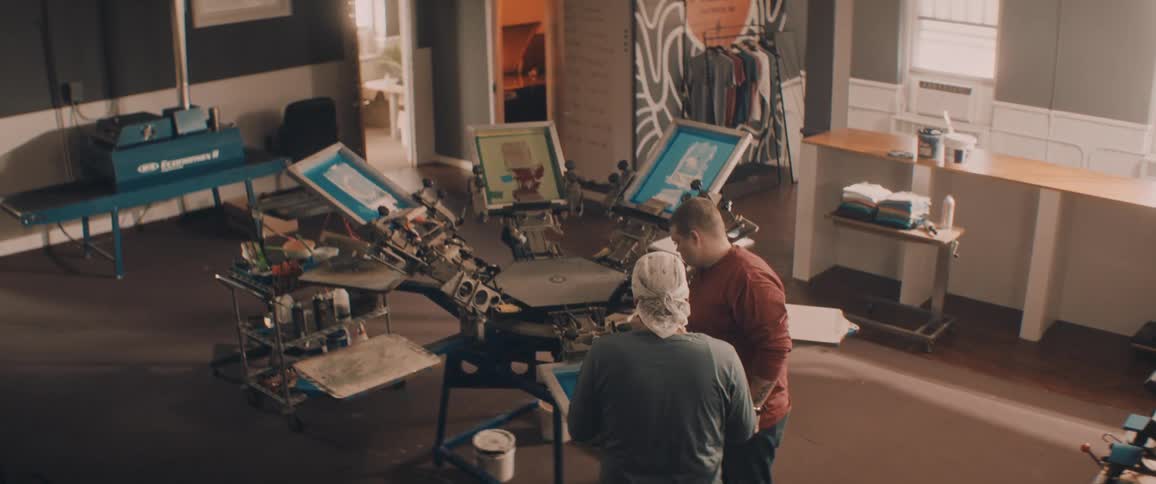 Two men adjusting a screen printing machine inside a workshop