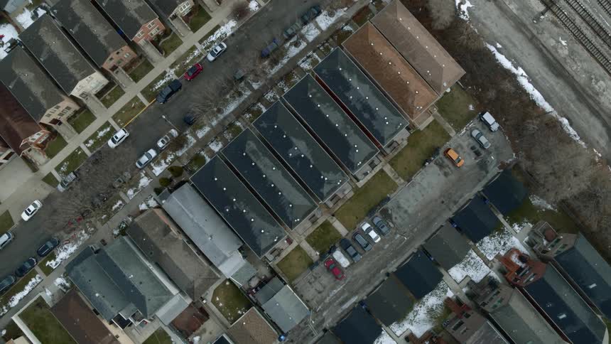 Aerial view of railroad tracks and streets in a neighborhood lined with houses and cars parked on the side of the road