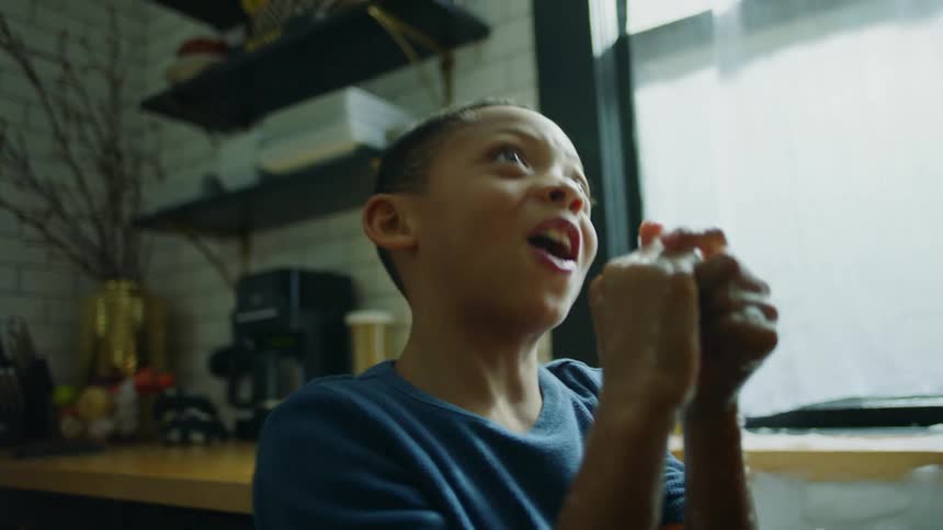 A boy laughs while soaping up his hands in the kitchen