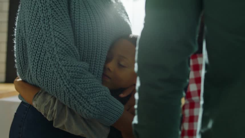 Mother hugs his son next to their family in the kitchen at home