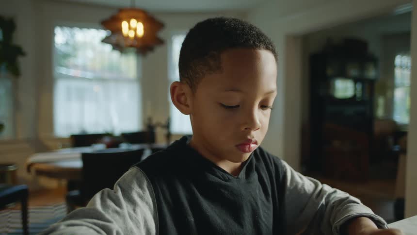 A young boy is sitting at a table looking down at something
