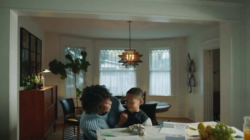 A mom hugs and kisses her son before picking up a marker to help him with his homework