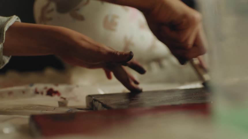 A child uses a sponge brush to paint on canvas while sitting on the floor