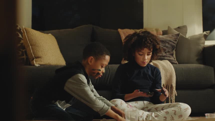 A girl spreads black paint on her fingers and hands as her brother paints beside her