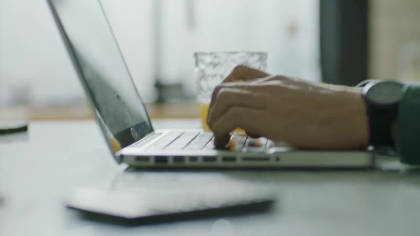 Person types on laptop near glass of juice