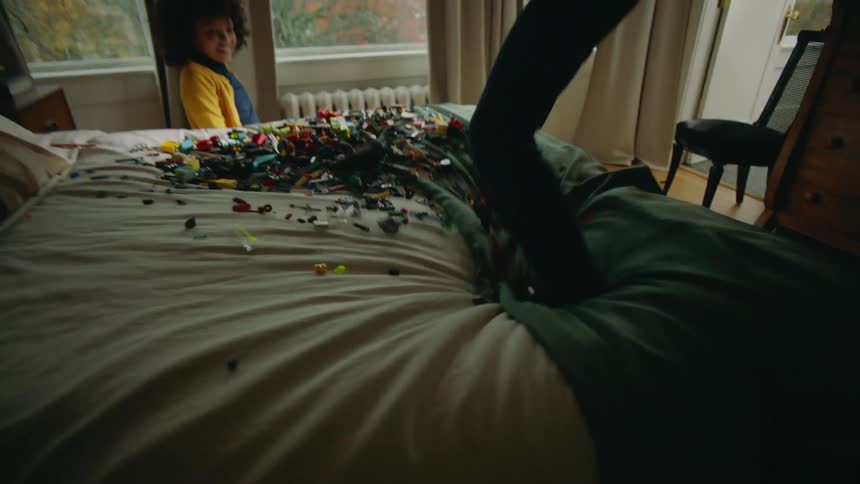 A boy pours a box of toys onto a bed before he and his sister begin jumping on the bed