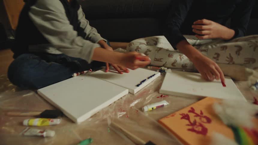Siblings paint sitting on plastic sheet on living room floor