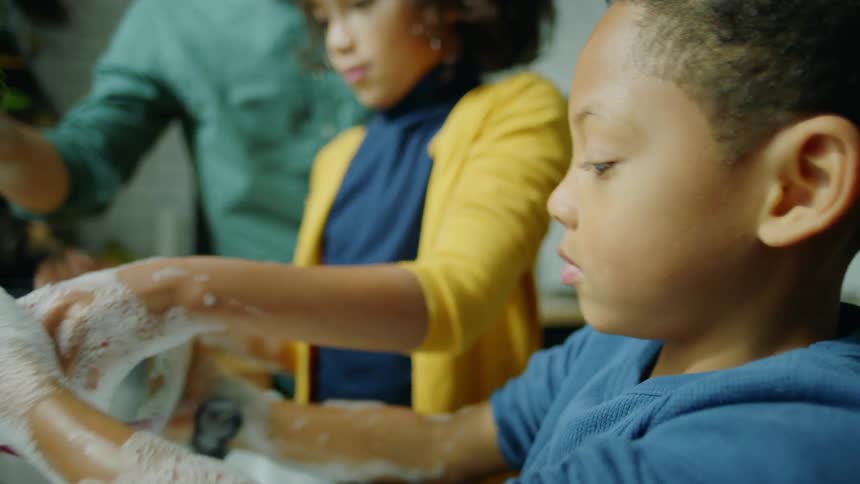 Father helps his children washing dishes on the kitchen sink at home