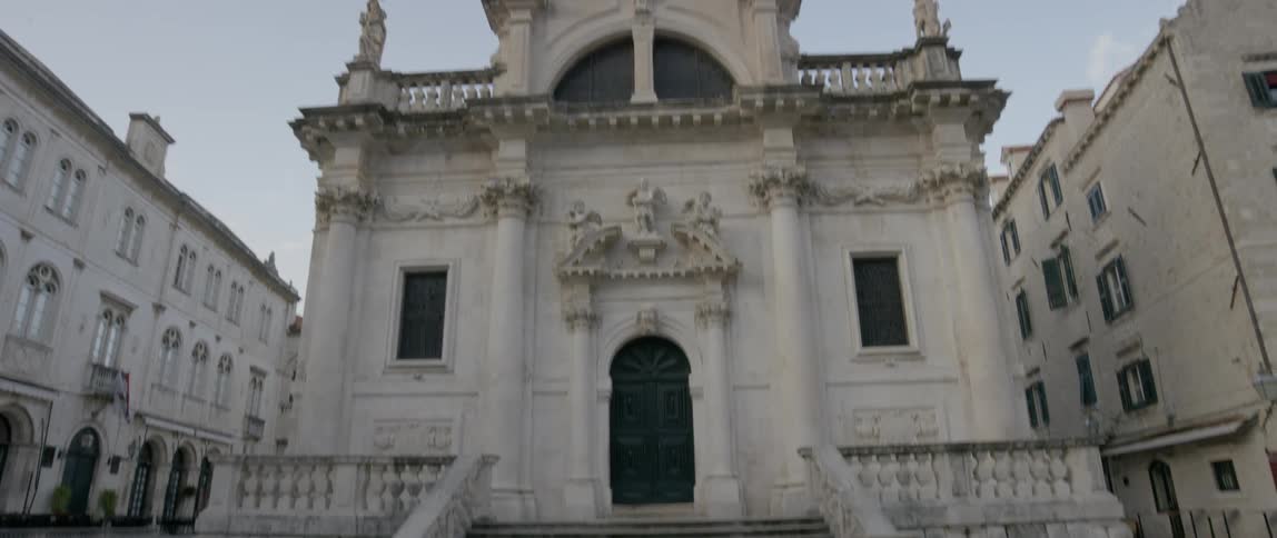 An old building with statues on top has pigeons at the base of its stairs