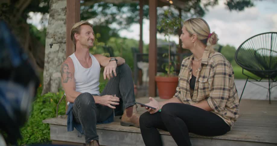 Young couple sitting on the porch talking while checking a phone at evening