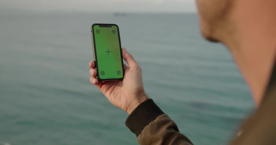 A man video chats on a smartphone while standing on the coast during the day