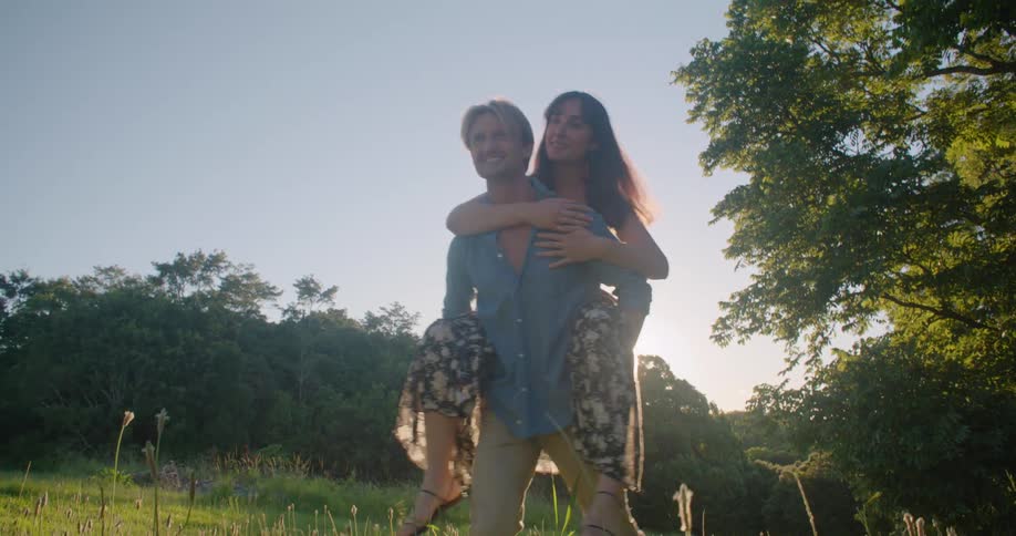 A man carries a woman piggyback as he walks across a field on a sunny day
