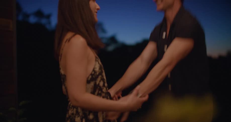 A woman dances with a man outdoors at night before being embraced by the man