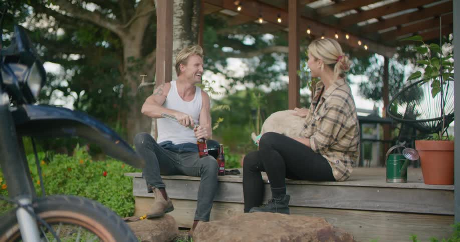 Woman sits petting dog and waiting for man to open beer bottle then takes a drink