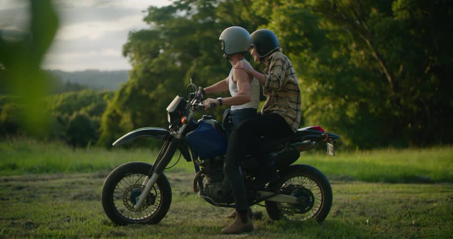 Young couple wearing helmets board a motorcycle on the countryside at sunset