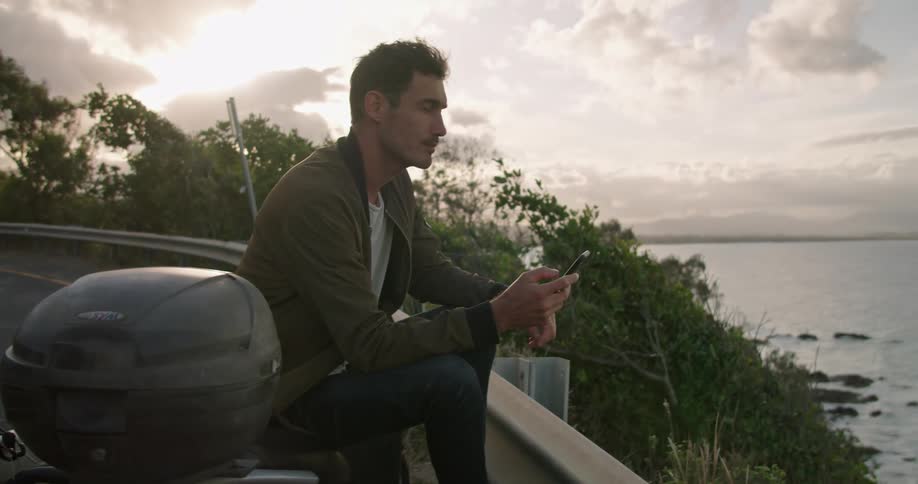 A man is sitting on his scooter on the road by the water