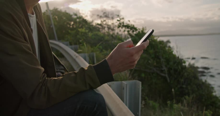 A man standing outdoors texting on a smartphone