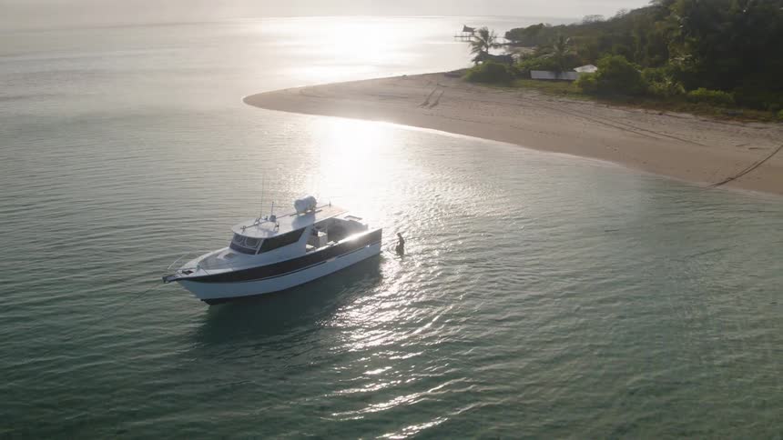 Aerial view of a person walking to a yatch on the shallow water next to the beach at sunset