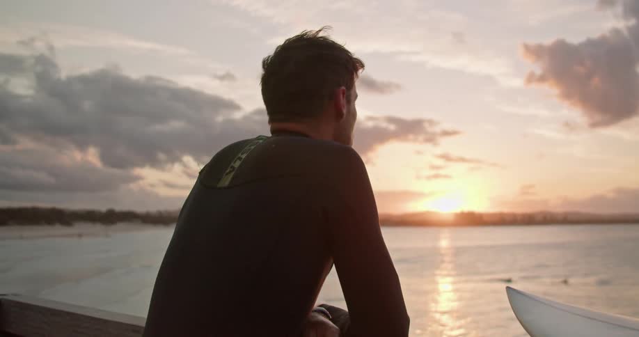 A man adjusts his wet suit and grabs his surfboard to head into the ocean