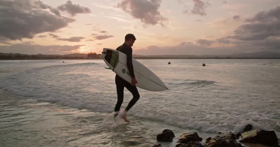 Surfer carries surfboard into ocean under red sky
