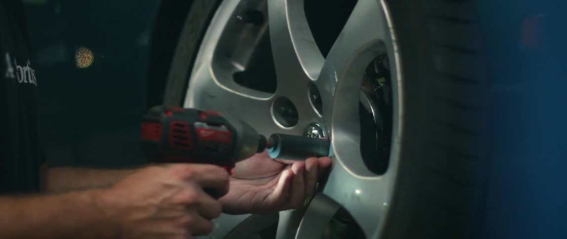A man is removing nuts on a tire with an air wrench inside an auto repair shop