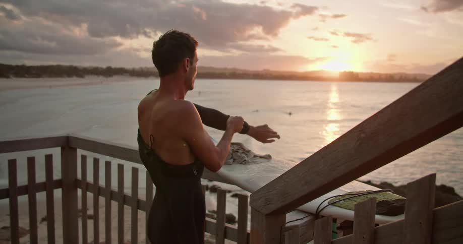 Man puts on wetsuit on the beach at sunset