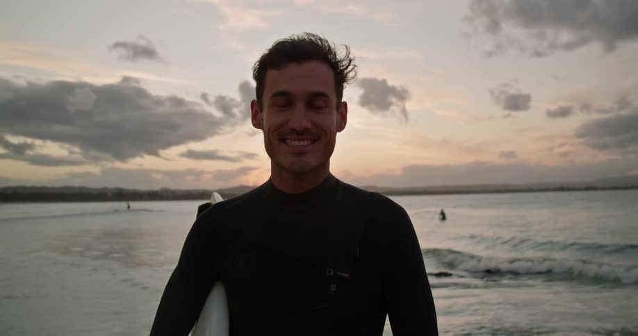 A man wearing a wetsuit is standing on a beach with the waves rolling in behind him