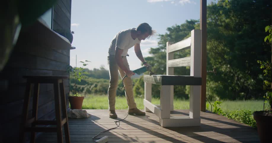 A man does carpentry work on a bench on a patio at a home