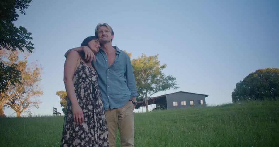 A man and woman stand on the grass by their home
