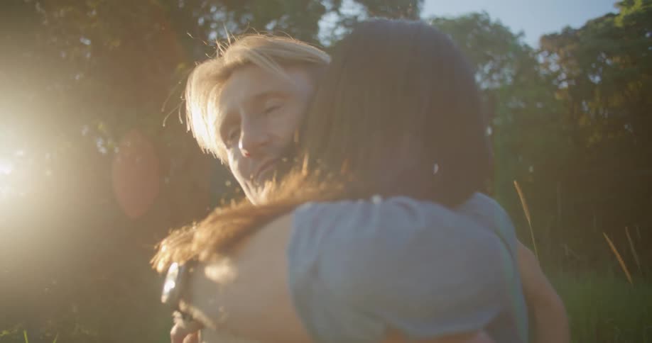 A man runs his hand through a womans hair before embracing her while standing outdoors during the day