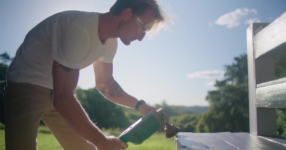 A man is using an electric sander on the bench