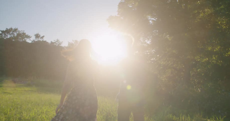 A man and woman holding hands running through the grass on a bright sunny day