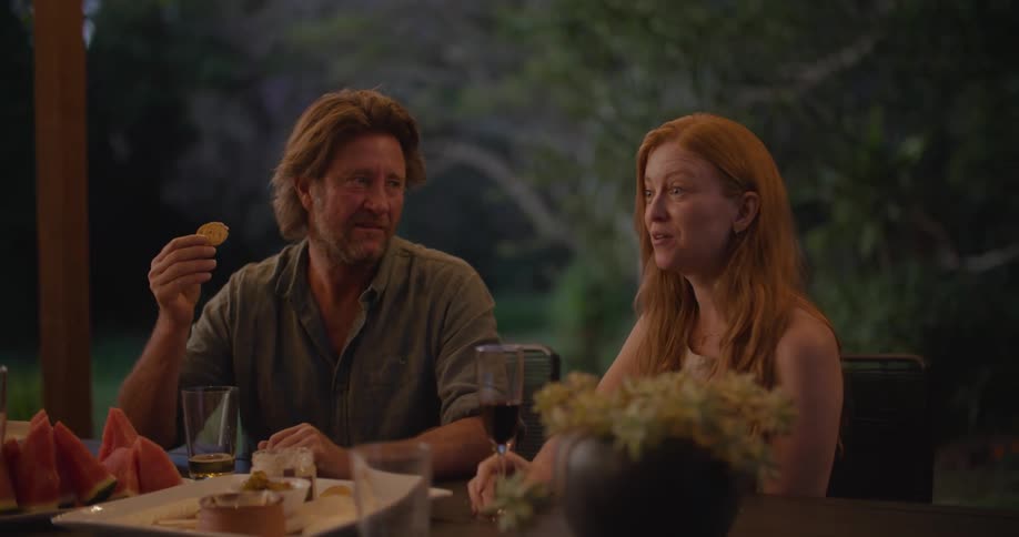 A group of people chat while eating together at a table in the evening