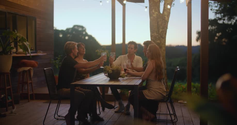 Group of friends toasting with wine on a table in the porch at sunset