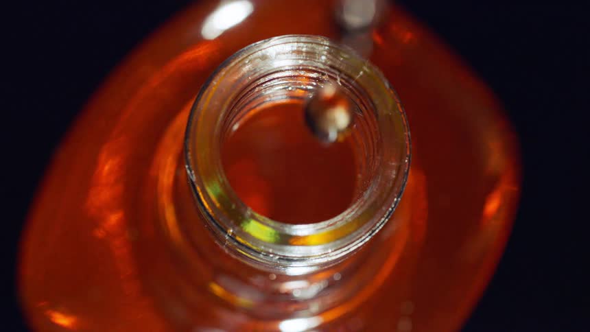 Top view of whiskey drop falling into a bottle as light turns on