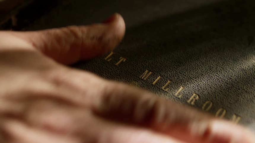 A man touches the cover of old leather distillery book