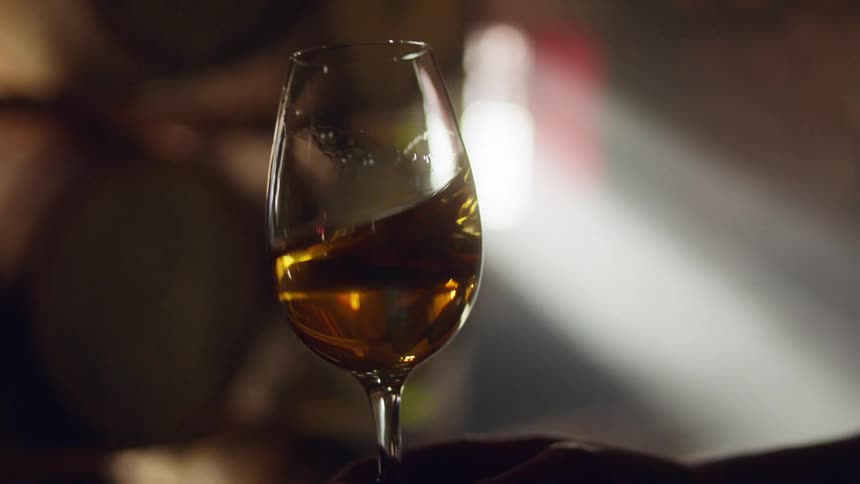 Person swirls wine in glass in dim room lit by sunlight from window