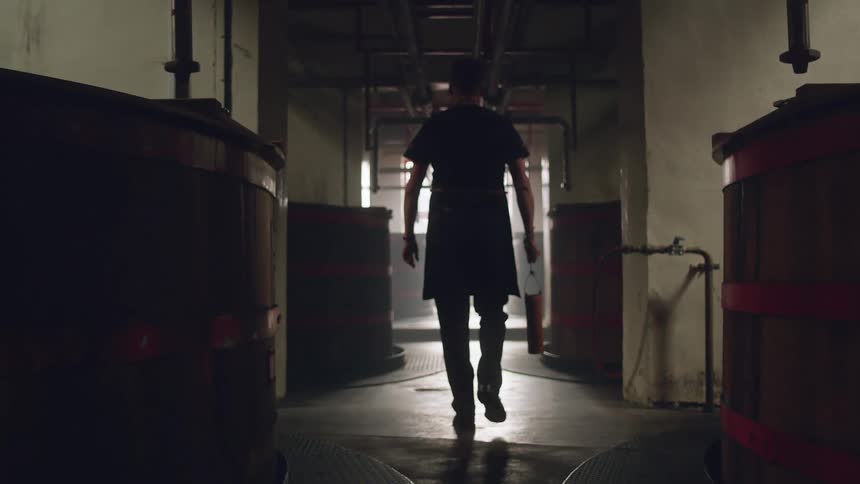 Silhouette of a distiller walking down a long dark hall in distillery