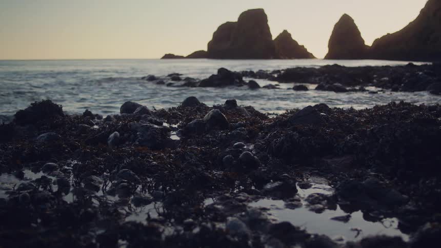 Waves roll in and water moves over rocks along the coast with large rock formations in the distance