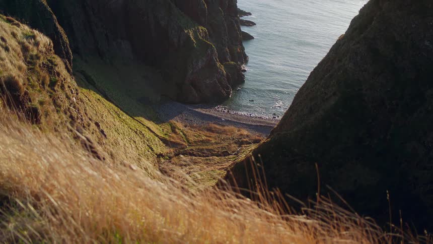 Ground slopes down toward beach between two steep cliffs on shore
