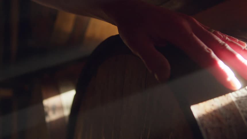 A man is tapping a barrel with a hammer in a cellar