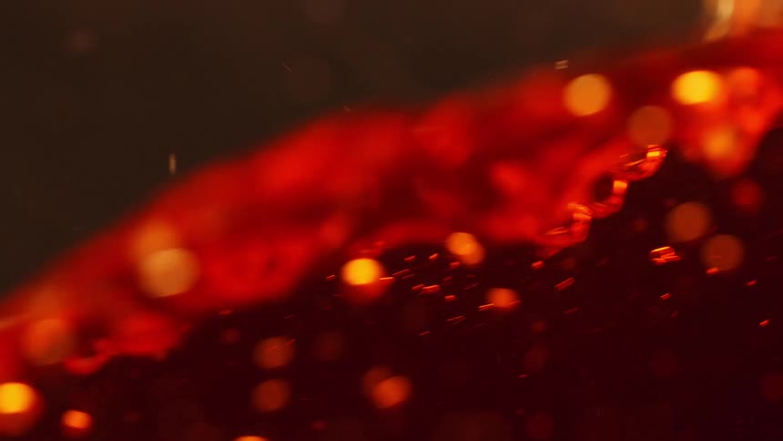 Close up of reddish liquor moving as drops fall into it and bubbles rise to the top