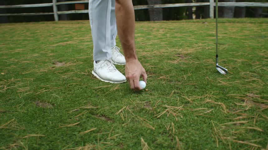 Man placing a golf ball over a tee in the green grass on a golf course