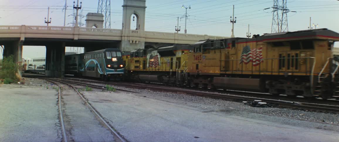 A cargo train and a passenger train cross paths under a bridge