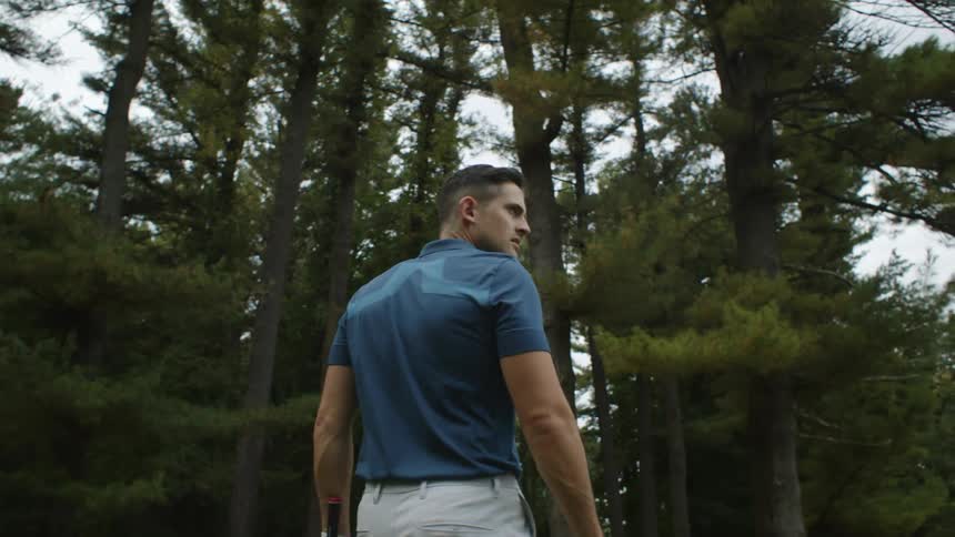 A golfer carries a golf club as he walks past a line of trees