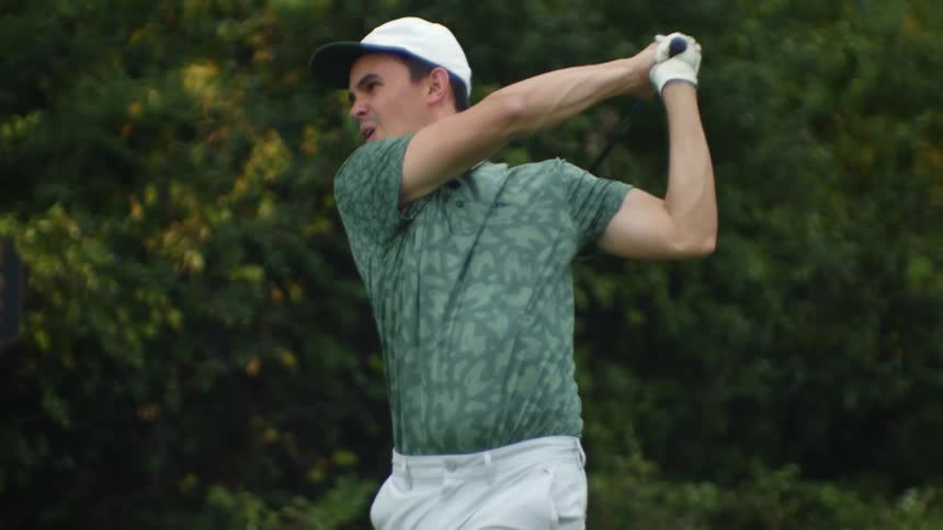 Man with white cap green polo shirt and white pants plays golf on golf course